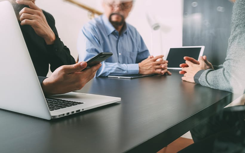 Three people at a desk holding phone