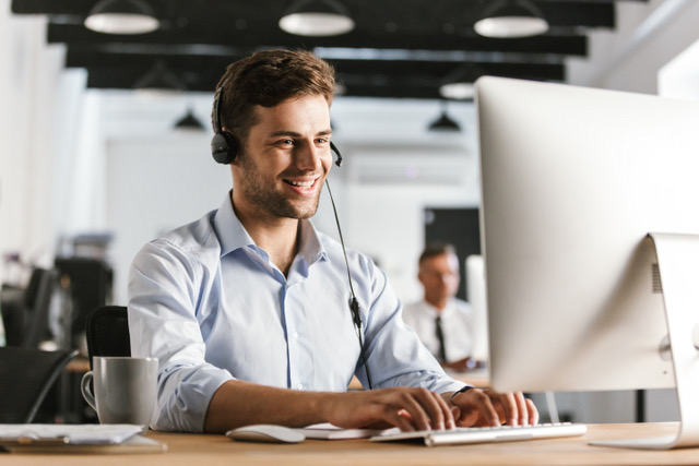 Photo of businesslike man 20s wearing office clothes and headset, working on computer in call center